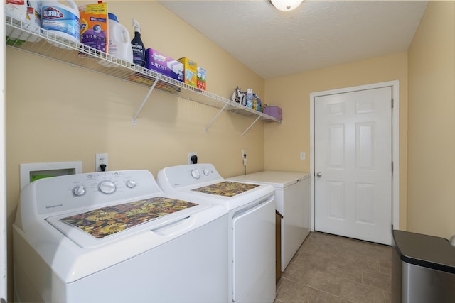 clothes washing area with laundry area, washing machine and dryer, light tile patterned floors, and a textured ceiling