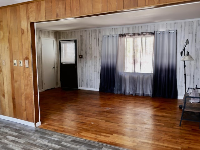 empty room featuring wood walls, wood finished floors, and baseboards