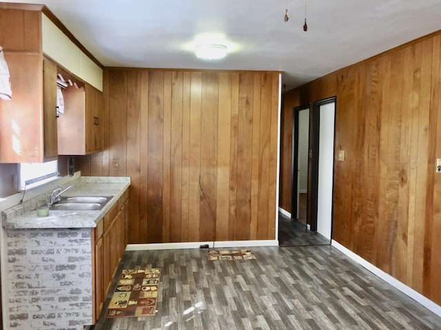 kitchen featuring wooden walls, wood finished floors, a sink, light countertops, and brown cabinetry