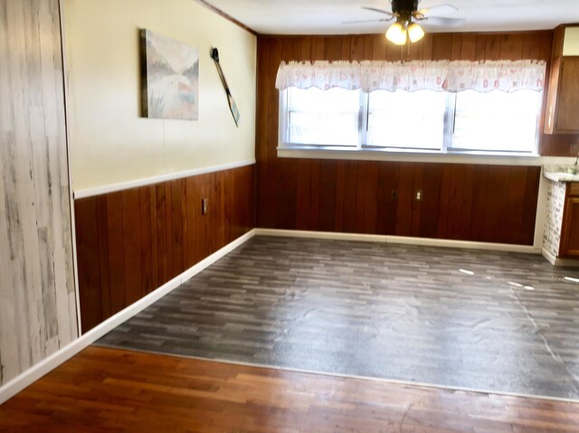 empty room featuring wainscoting, wood walls, a ceiling fan, and wood finished floors