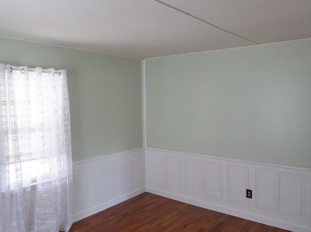 unfurnished room with dark wood finished floors, a wealth of natural light, and wainscoting