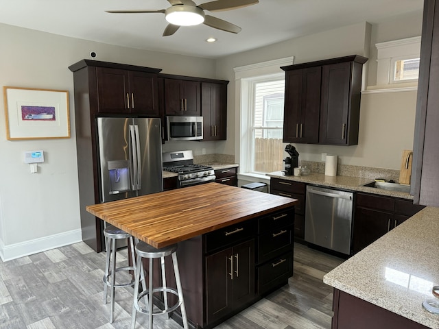 kitchen with a breakfast bar area, light wood finished floors, stainless steel appliances, wood counters, and baseboards