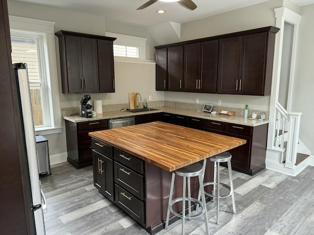 kitchen with appliances with stainless steel finishes, a sink, wood counters, dark brown cabinets, and light wood-type flooring