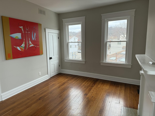 empty room with hardwood / wood-style flooring, baseboards, visible vents, and a wealth of natural light