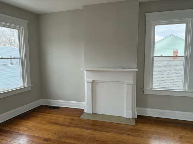 unfurnished living room with wood-type flooring, visible vents, and baseboards