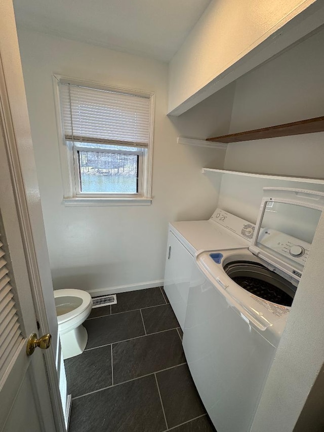 clothes washing area featuring visible vents, baseboards, laundry area, washer and dryer, and dark tile patterned flooring