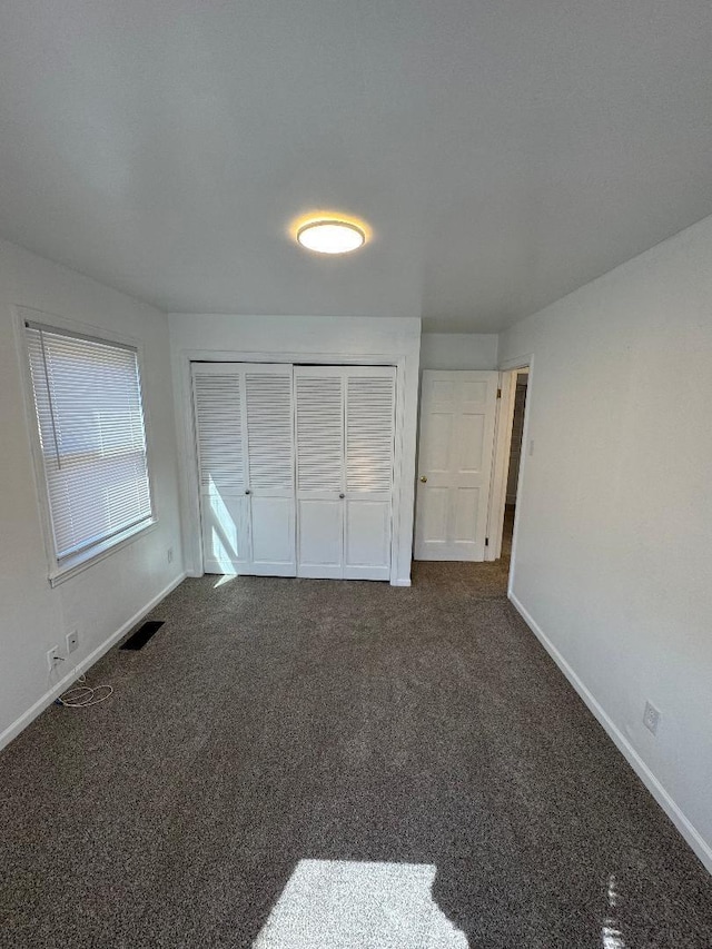 unfurnished bedroom with visible vents, baseboards, a closet, and dark carpet