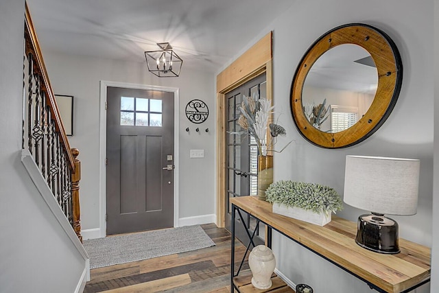 foyer entrance featuring a notable chandelier, stairs, baseboards, and wood finished floors