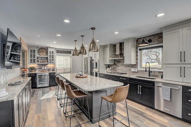 kitchen featuring wall chimney range hood, wine cooler, a breakfast bar, stainless steel appliances, and a sink