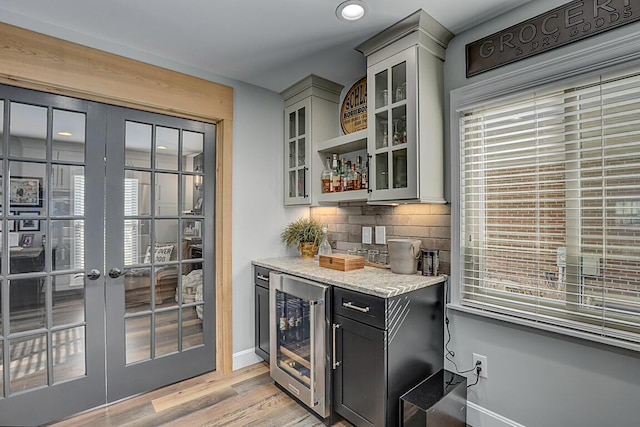 bar with light wood-style flooring, a bar, decorative backsplash, wine cooler, and french doors