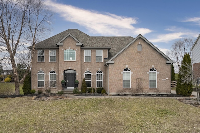 colonial inspired home featuring a shingled roof, a front lawn, and brick siding