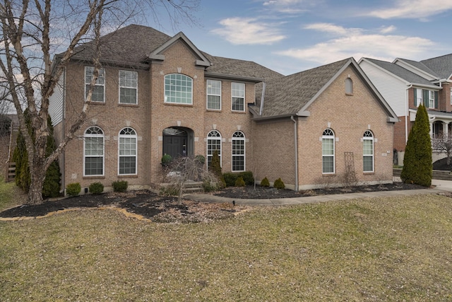 colonial-style house featuring roof with shingles, a front yard, and brick siding