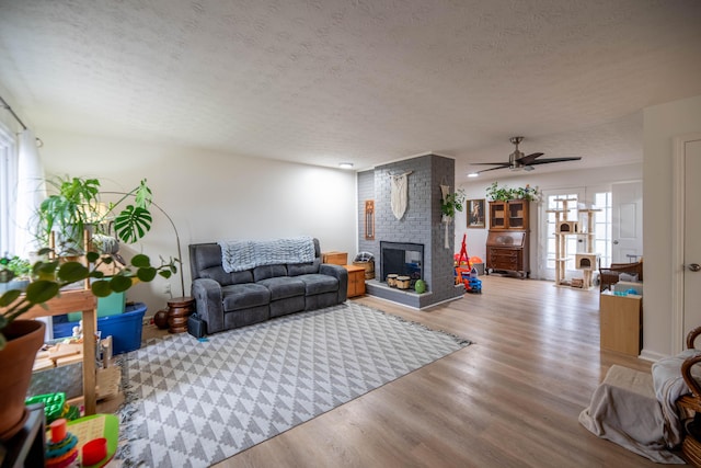 living area featuring a fireplace, ceiling fan, wood finished floors, and a textured ceiling