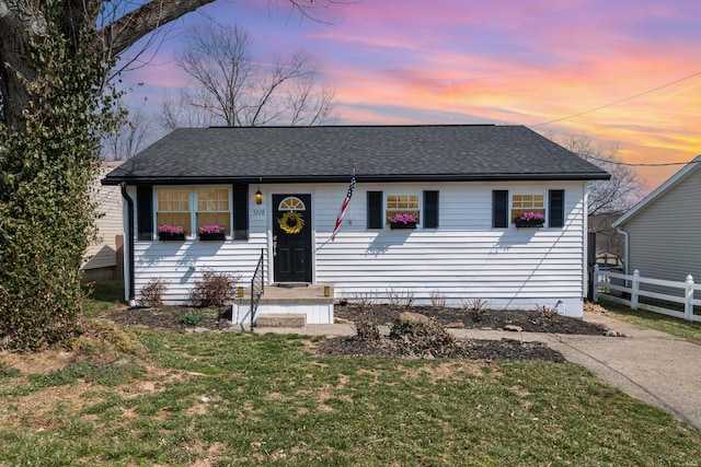 view of front of property with a lawn, roof with shingles, and fence