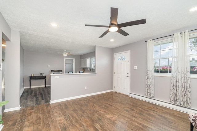 unfurnished living room with baseboards, ceiling fan, baseboard heating, dark wood-style floors, and a textured ceiling