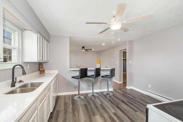 kitchen featuring a breakfast bar, a sink, a baseboard heating unit, a textured ceiling, and dark wood finished floors