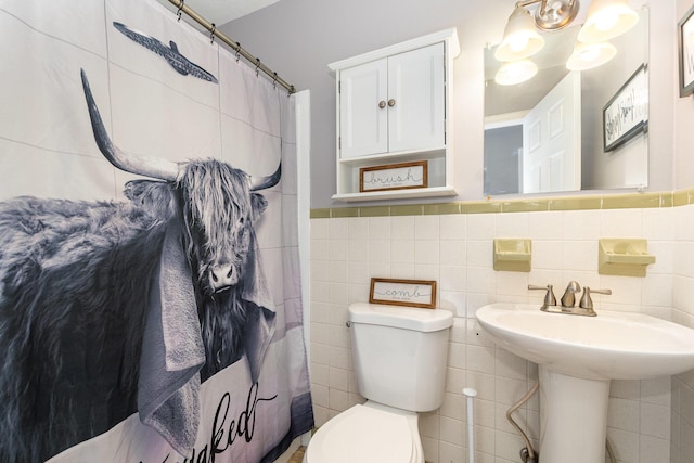 bathroom with wainscoting, curtained shower, toilet, and tile walls