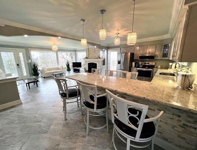 kitchen featuring a large fireplace, appliances with stainless steel finishes, ornamental molding, a peninsula, and a sink