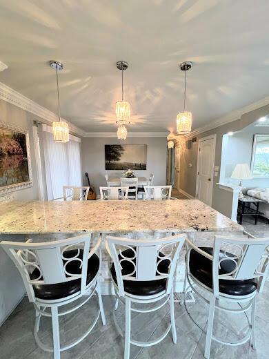 kitchen with pendant lighting, ornamental molding, a breakfast bar area, and light stone countertops