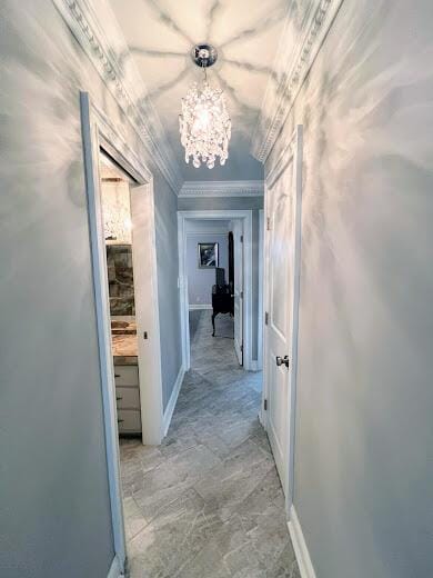 hall featuring baseboards, ornamental molding, and an inviting chandelier