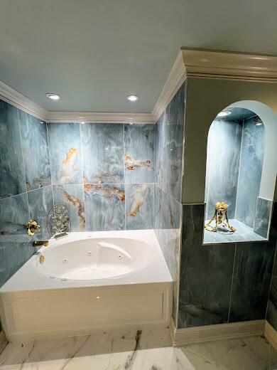 bathroom with ornamental molding, marble finish floor, and a tub with jets