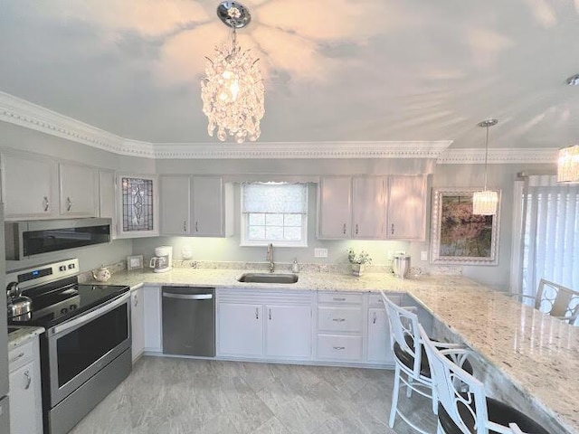 kitchen featuring light stone counters, hanging light fixtures, appliances with stainless steel finishes, ornamental molding, and a sink