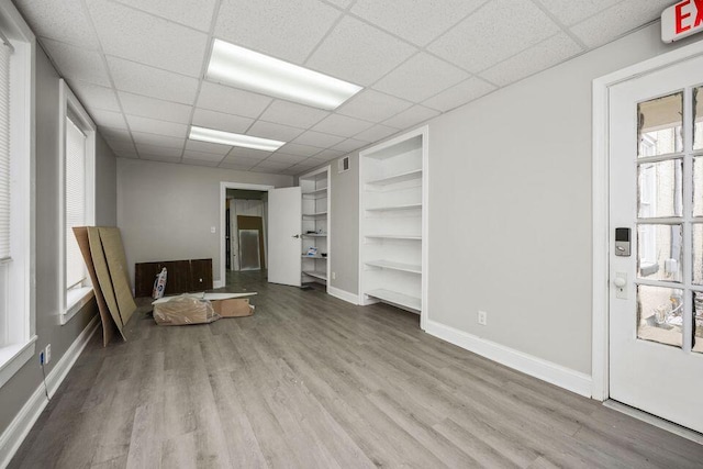 interior space featuring visible vents, a drop ceiling, baseboards, and wood finished floors