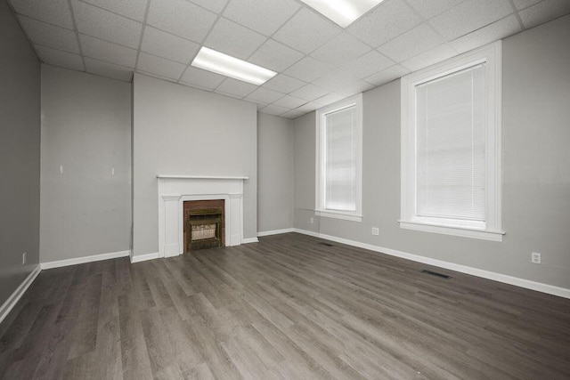 unfurnished living room with visible vents, baseboards, dark wood-type flooring, a paneled ceiling, and a fireplace