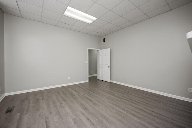 spare room featuring a paneled ceiling, visible vents, baseboards, and wood finished floors