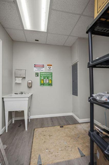 interior space with a paneled ceiling, electric panel, baseboards, and wood finished floors