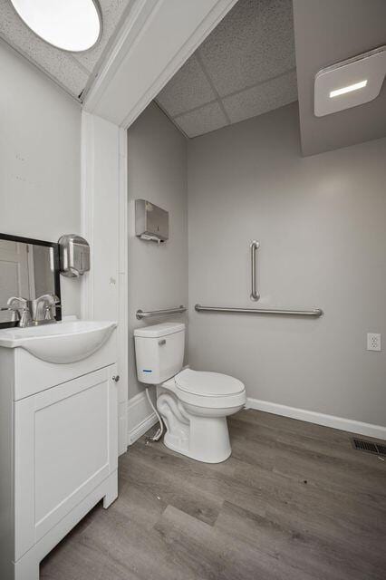 half bath featuring toilet, a paneled ceiling, wood finished floors, vanity, and baseboards