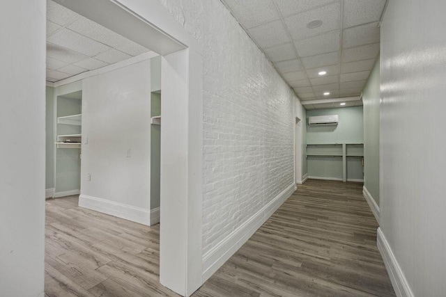 hallway featuring a paneled ceiling, an AC wall unit, brick wall, and wood finished floors