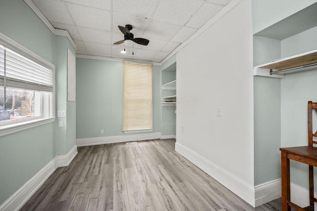 interior space featuring ceiling fan, baseboards, a drop ceiling, and wood finished floors