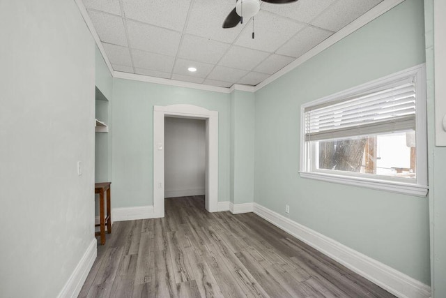 unfurnished bedroom with a paneled ceiling, baseboards, wood finished floors, and ornamental molding