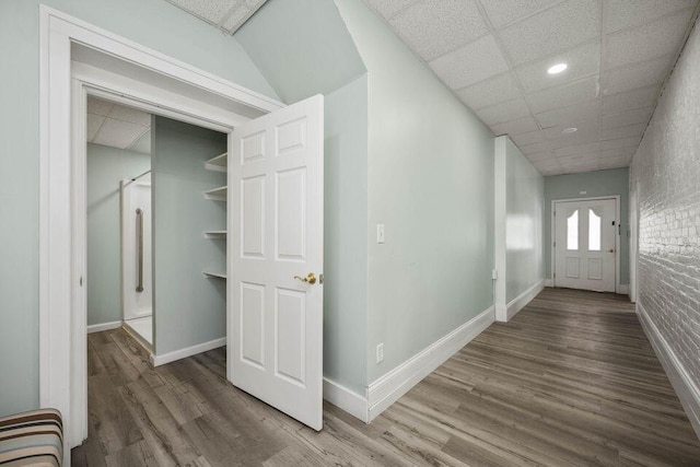 corridor with baseboards, a drop ceiling, brick wall, wood finished floors, and recessed lighting