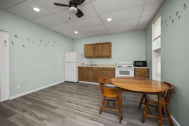 kitchen featuring white appliances, baseboards, brown cabinets, wood finished floors, and a sink