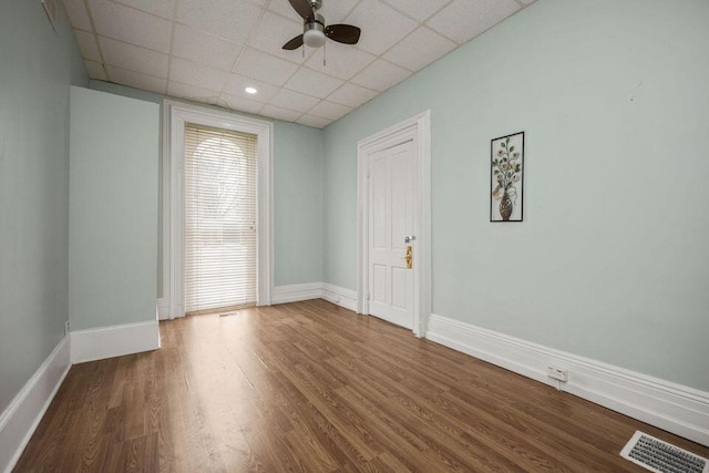 empty room with a ceiling fan, wood finished floors, visible vents, and baseboards