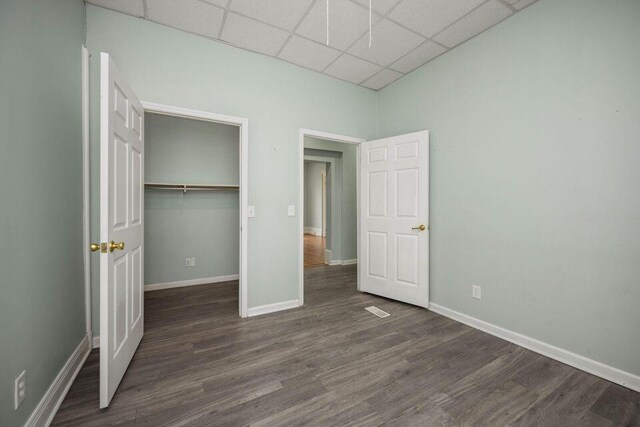 unfurnished bedroom with a closet, a drop ceiling, wood finished floors, and baseboards