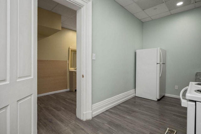 kitchen with white appliances, a drop ceiling, dark wood finished floors, and baseboards