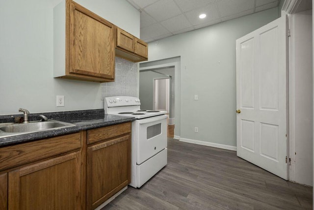 kitchen with dark wood-type flooring, a sink, brown cabinetry, white range with electric cooktop, and dark countertops