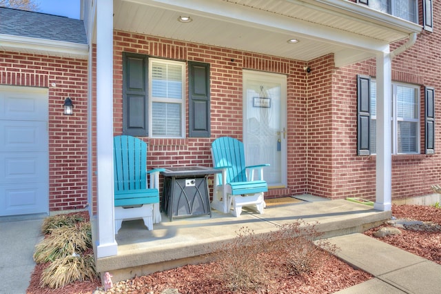 doorway to property featuring a garage, brick siding, and a porch