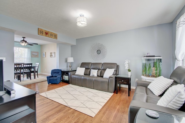 living area featuring ceiling fan, baseboards, and light wood-style flooring