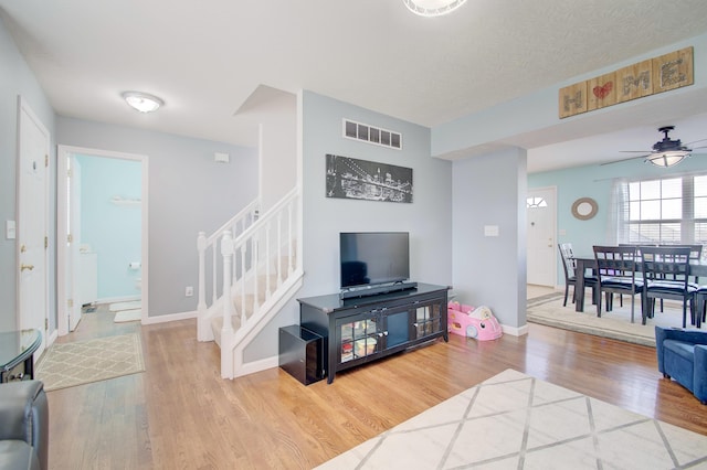 living room with a ceiling fan, wood finished floors, visible vents, baseboards, and stairs