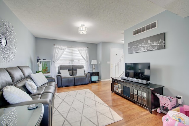 living room featuring baseboards, visible vents, light wood finished floors, stairs, and a textured ceiling