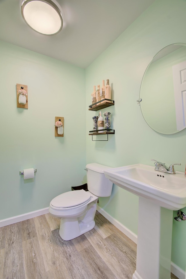 half bathroom with a sink, toilet, baseboards, and wood finished floors