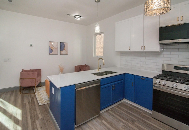 kitchen featuring blue cabinets, a peninsula, a sink, appliances with stainless steel finishes, and tasteful backsplash