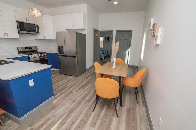 kitchen with white cabinets, decorative backsplash, appliances with stainless steel finishes, light countertops, and light wood-type flooring