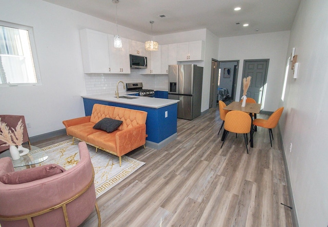 kitchen with white cabinets, a peninsula, a sink, stainless steel appliances, and backsplash