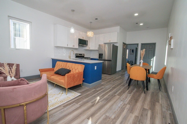 kitchen with light wood finished floors, decorative backsplash, appliances with stainless steel finishes, a peninsula, and white cabinetry