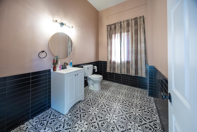 bathroom featuring toilet, tile walls, wainscoting, tile patterned flooring, and vanity